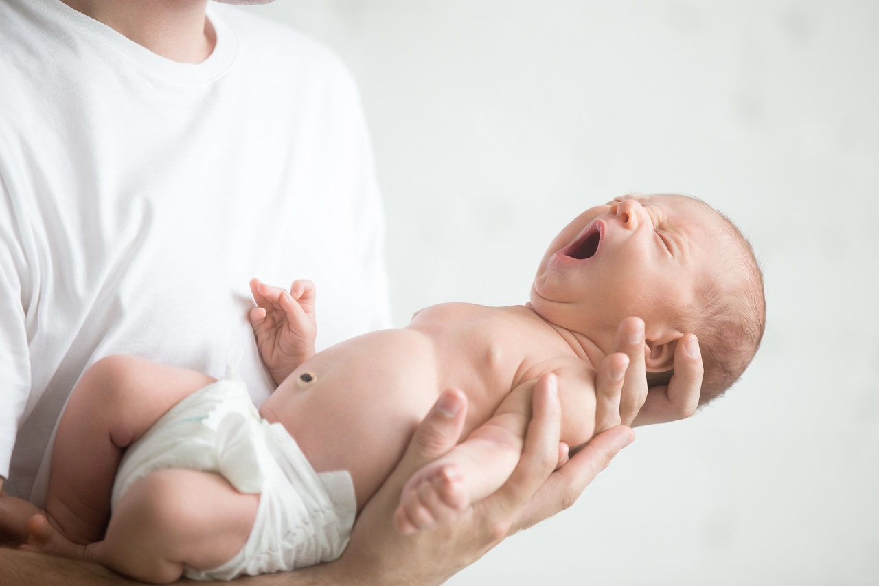 A person in white wearing a newborn baby in diapers yawning