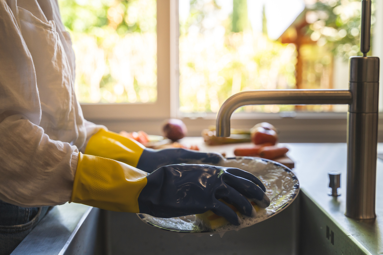 A woman cleaning the dishes with gloves on